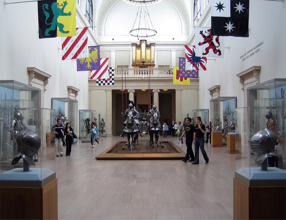 This photograph shows four mounted Knights at the Arms and Armor Department at the Metropolitan Museum of Art in New York. It also shows a collection of various pieces of arms and armor.