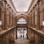 This photograph shows a colonnaded staircase known as the Grand Stairway that leads down to the Great Hall at the The Metropolitan Museum of Art in New York City.