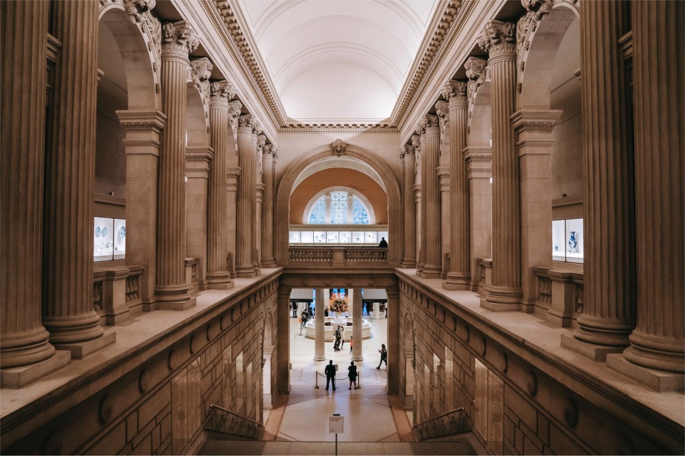 This photograph shows a colonnaded staircase known as the Grand Stairway that leads down to the Great Hall at the The Metropolitan Museum of Art in New York City.